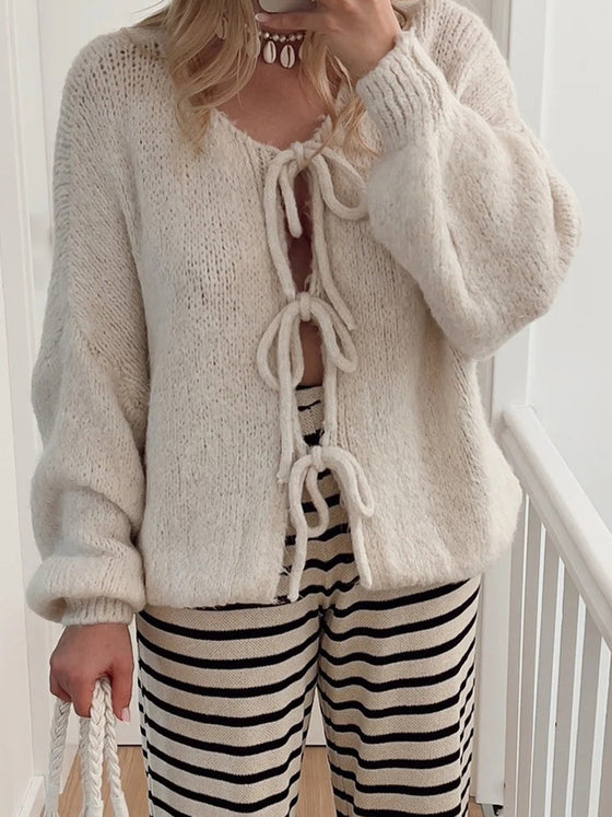 Front view of a woman wearing a Tied Long Sleeve Dropped Shoulder Cardigan in a soft beige color, paired with striped knit pants for a casual-chic look.