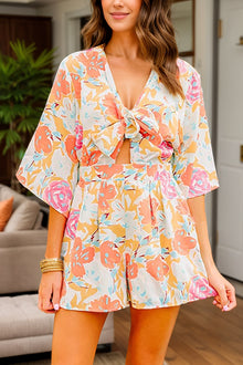  Woman wearing a vibrant floral printed half-sleeve romper with a tied front, styled for a casual, chic look.

