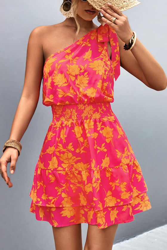 Model wearing a Tied Smocked Printed Single Shoulder Dress with pink and red floral print, smocked waist, and tiered hem, perfect for summer outings.

