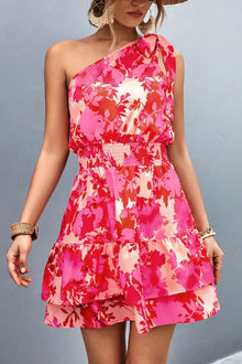  Model wearing a Tied Smocked Printed Single Shoulder Dress with pink and red floral print, smocked waist, and tiered hem, perfect for summer outings.

