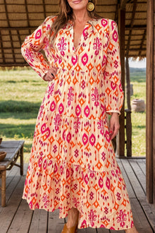  Woman wearing a vibrant tiered printed midi dress with a notched neckline and long sleeves, styled for an elegant outdoor setting.

