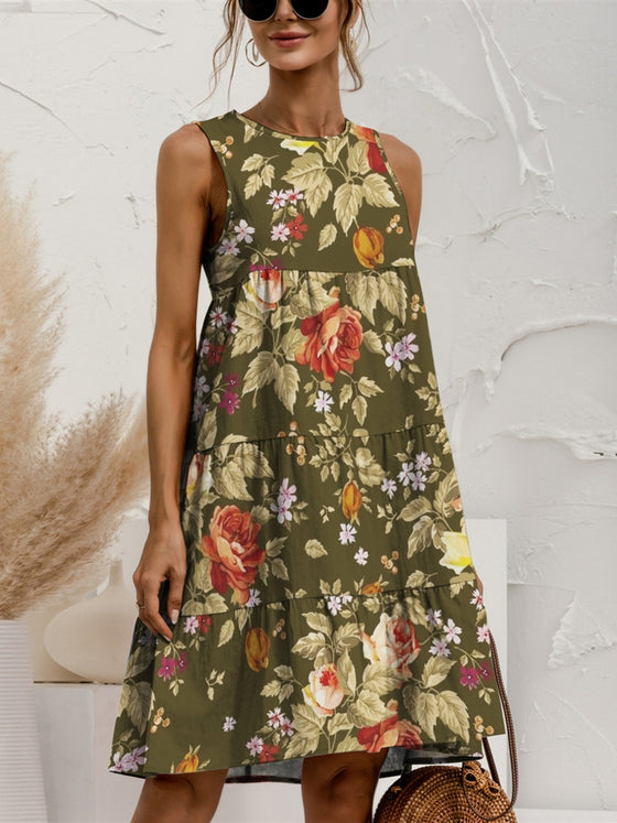 Woman wearing a floral Tiered Printed Round Neck Sleeveless Dress in soft earthy tones, styled with a woven bag and casual accessories, perfect for a sunny day.