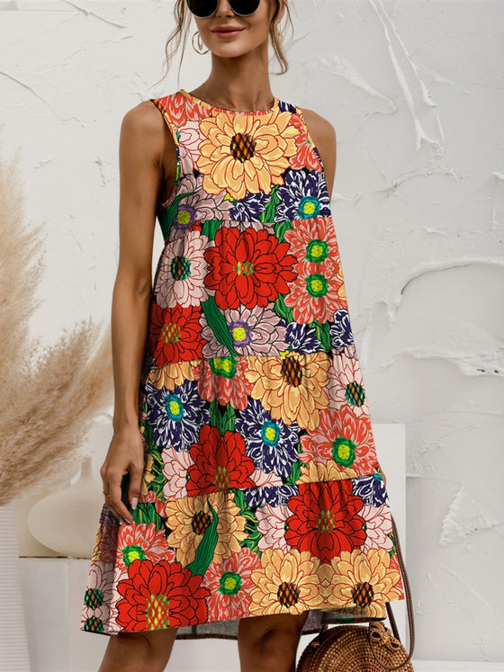 Woman wearing a floral Tiered Printed Round Neck Sleeveless Dress in soft earthy tones, styled with a woven bag and casual accessories, perfect for a sunny day.