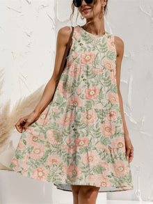  Woman wearing a floral Tiered Printed Round Neck Sleeveless Dress in soft earthy tones, styled with a woven bag and casual accessories, perfect for a sunny day.