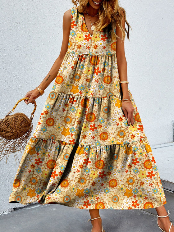 Woman wearing a vibrant Tiered Printed V-Neck Sleeveless Dress with colorful paisley-inspired print, accessorized with a straw bag and sandals.