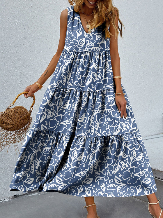 Woman wearing a vibrant Tiered Printed V-Neck Sleeveless Dress with colorful paisley-inspired print, accessorized with a straw bag and sandals.