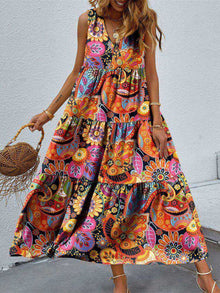  Woman wearing a vibrant Tiered Printed V-Neck Sleeveless Dress with colorful paisley-inspired print, accessorized with a straw bag and sandals.