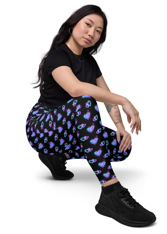 Side view of a woman sitting while wearing Vibrant Neon Heart black high-waisted leggings with pockets. Perfect for yoga, gym, or casual wear. High-rise compression leggings with a sleek design and bold neon heart print.