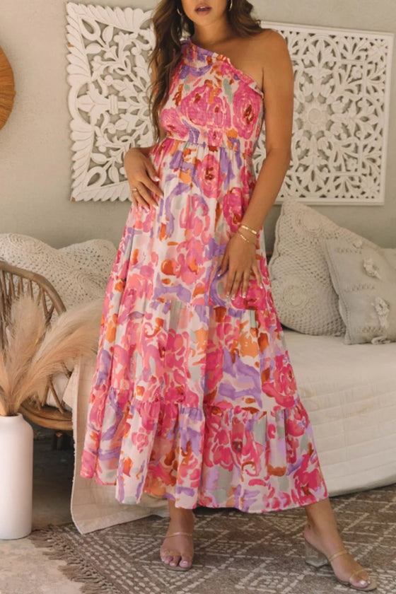 Full-length front image capturing the romantic one-shoulder detail and the elegant fall of the floral printed fabric.

