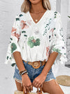 White blouse featuring elegant floral patterns and half-length sleeves, worn front-facing with a tucked-in look.