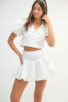  Model wearing a chic white two-piece outfit featuring a fitted top and voluminous bubble skirt in a crisp, modern front view.