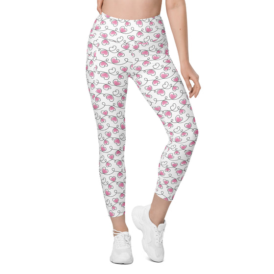 Model standing in full front pose wearing white heart print leggings. Women's high waist leggings with side pockets and compression fit.
