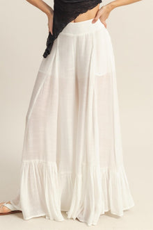 Front view of white ruffle-trimmed wide-leg pants styled with a minimal top, perfect for elegant daywear or resort looks.
