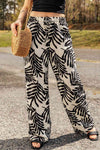 Model wearing printed drawstring waist pants with a bold black and white leaf pattern, paired with a black top and straw bag for a casual outdoor look.