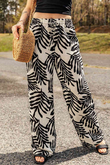  Model wearing printed drawstring waist pants with a bold black and white leaf pattern, paired with a black top and straw bag for a casual outdoor look.