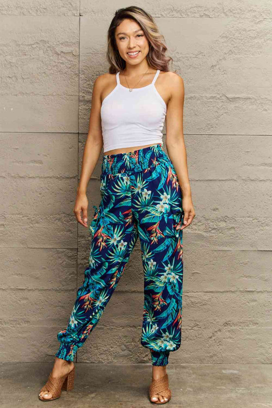 Model wearing the smocked plant print long pants in a casual setting, perfect for beach outings and tropical-inspired looks.
